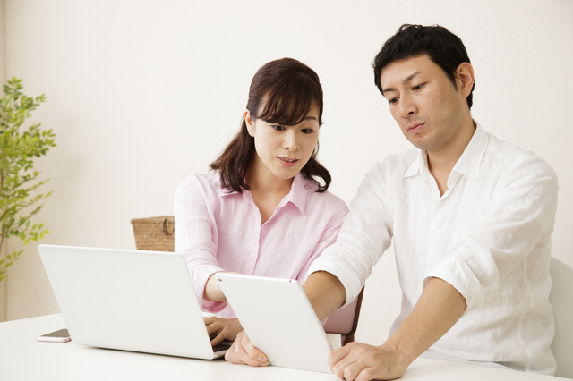 ノートパソコンとタブレットを見ながら考える夫婦