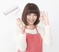 赤いエプロンをして掃除道具を持ち、OKマークを出して笑顔の女性